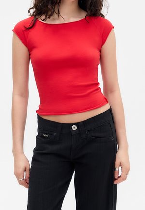 Woman wearing a fitted, short-sleeve red crop top paired with high-waisted black pants, showing midriff and ring accessories on fingers.