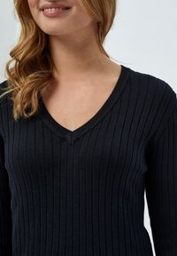 Schwarzer gerippter Strickpullover mit tiefem V-Ausschnitt und langen Ärmeln, ausgestattet mit vertikalen Streifen für Struktur und einer figurbetonten Silhouette.