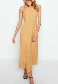 Senapsgul maxiklänning med halterneck-design, som har en nyckelhålsutskärning och mörkbruna detaljer vid halslinningen. Slät textur.