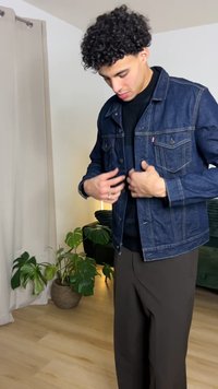 Medium wash denim jacket with button closures, two front pockets, and contrast stitching. Worn over a black top, paired with brown pants.