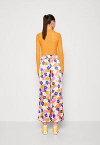 Top de encaje naranja de manga larga combinado con pantalones de flores de pierna ancha que presentan flores rosas, amarillas y azules. Sandalias amarillas de tacón grueso.