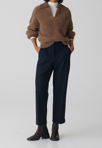 Brun fluffig tröja med V-ringning och krage, parat med marinblå skräddarsydda byxor. Mörkbruna ankelboots fulländar outfiten.