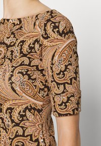Nära bild av en brun topp med korta ärmar som har ett intrikat paisleymönster i orange, beige och vitt på tyget.