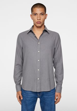 Grå langærmet skjorte med knaplukning, klassisk krave og subtil struktur. Sammen med blå jeans, der har lige pasform.