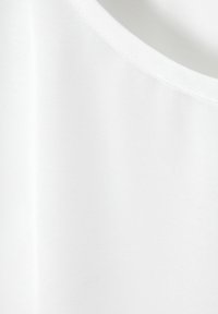 Top sin mangas blanco hecho de una tela suave y ligera. Presenta un escote redondo y un diseño sin costuras. La textura parece suave y uniforme.