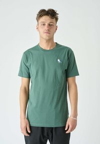 Grünes Baumwoll-T-Shirt mit Rundhalsausschnitt, kurzen Ärmeln und einer kleinen blau-weißen Vogelstickerei auf der linken Brust.