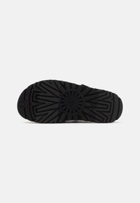 Suola di scarpa nera con un motivo geometrico testurizzato e un logo circolare al centro, progettata per la trazione e la durabilità.