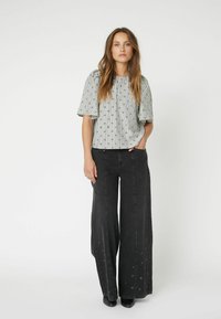 Blusa a righe, con maniche corte, in grigio e bianco, abbinata a jeans neri a vita alta e gamba larga con dettagli in grommet argento.