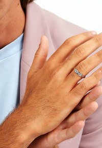 Silver ring med en vriden design på ringfingret, hålls mot en hand med ljus hy och kort hår, klädd i en blazer i rosafärg.