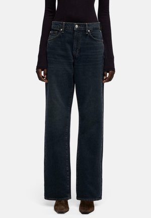 Donkerblauwe, high-waist jeans met wijde pijpen, voorzien van het klassieke ontwerp met vijf zakken, metalen knoopsluiting en subtiele vervaging, gedragen door een model.