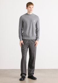 Pulover gri tricotat cu guler cu nervuri și un logo mic, asortat cu pantaloni gri cu model și pantofi slip-on negri.