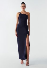 Tamsiai mėlyna, viena petneša satino suknelė su kojų aukščio skeltuku ir prigludusia forma. Pabrėžia kūno siluetą su minimaliais aksesuarais.