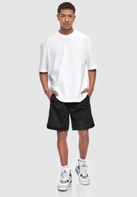 Hvid bomulds t-shirt med korte ærmer, parret med sorte mesh shorts. Outfittet er komplementeret af hvide sneakers med sorte accenter.