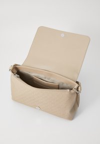 Beige crossover taske med en tekstureret overflade, lynlås lukning og magnetisk snap. Indvendigt har den et logo mønster og flere rum.