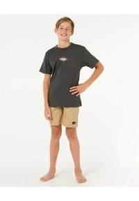 Camiseta gris con un gráfico de ojo colorido, combinada con pantalones cortos beige. El tejido parece ligero; los pantalones cortos tienen una pequeña etiqueta de logo negra.