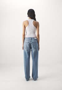 Top sin mangas blanco combinado con jeans de tiro alto y pierna ancha en azul claro. Los jeans tienen bolsillos traseros y detalles de costura sutiles.