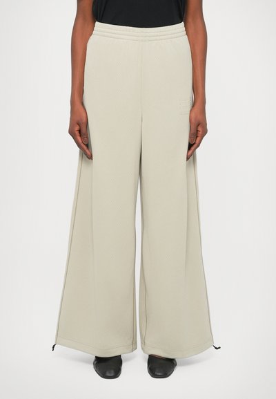 Pantalons larges gris clair en tissu texturé, avec une taille côtelée et des accents noirs au bas.
