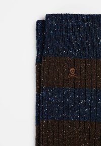 Calcetines de punto con un patrón a rayas en marrón oscuro y azul, confeccionados con hilo texturizado, que incluyen un pequeño logo de calavera en marrón.
