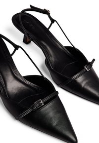 Décolleté in pelle nera con punta affusolata, cinturini sottili e piccolo dettaglio con fibbia argentata sul davanti. Soletta e tacco texture.