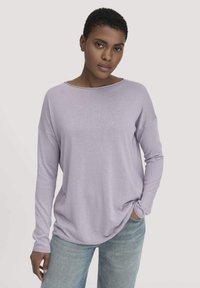 Hellviolettes Langarmshirt mit weitem Ausschnitt, lockerer Passform und gerippten Bündchen, kombiniert mit hellblauen Jeans. Weiche Textur.