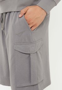 Grå bomullsshorts med dragsko i midjan, sidficka och ficka med klaff med sydda detaljer på tyget.