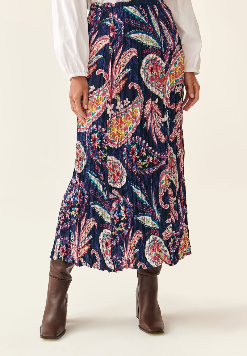 Larga falda azul marino con coloridos patrones florales y de paisley, que presenta un diseño plisado y un dobladillo que se ensancha. Botas marrones hasta la rodilla.