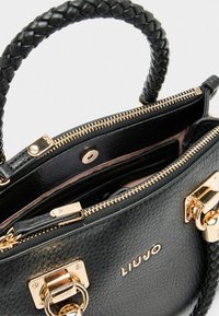 Sac à main en cuir noir avec une finition texturée, une anse tressée, des accents en métal doré et une fermeture à glissière. Intérieur visible avec des poches.