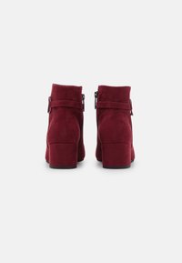 Bottines en nubuck bordeaux avec un talon carré. Présentent une large sangle et des accents en métal argenté. Texture lisse, design minimaliste.