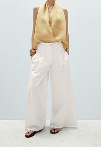 Pantalon large blanc avec des plis et une ceinture. Associé à un haut sans manches jaune, ample et en tissu léger. Coupe simple et décontractée.