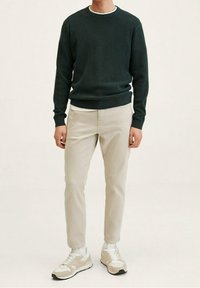 Ciemnozielony sweter o fakturze, jasnobeżowe spodnie typu slim-fit oraz beżowe trampki z białymi akcentami. Prosty, okrągły dekolt i ściągacze na rękawach.