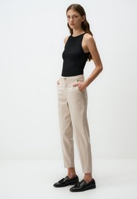 Bodysuit noir sans manches, pantalon taillé beige taille haute avec poches, tissu lisse, associé à des mocassins noirs. Design simple et élégant.