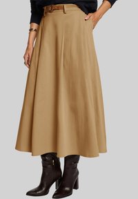 Une jupe midi beige plissée, dotée d'une ceinture tan, accompagnée de bottes en cuir marron montant jusqu'aux genoux, avec un bout pointu et un talon bloc.