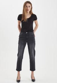 Top noir côtelé avec de courtes manches bouffantes, associé à un jean noir délavé taille haute avec cinq poches et ourlets retroussés. Élégantes escarpins noirs.