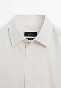 Chemise blanche en coton avec col pointu et boutonnage sur le devant, affichant l'étiquette de la marque à l'intérieur du col.