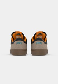 Sneakers w kolorze brązowym i czarnym z teksturowaną cholewką, pomarańczowym wykończeniem oraz niebieskim logo "Etnies" na pięcie, z gumową podeszwą.