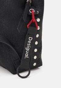 Czarna torebka o fakturowanej powierzchni z srebrnymi ćwiekami i czerwonym akcentem. Posiada metkę z napisem "Desigual" oraz boczne kółko do przymocowania.