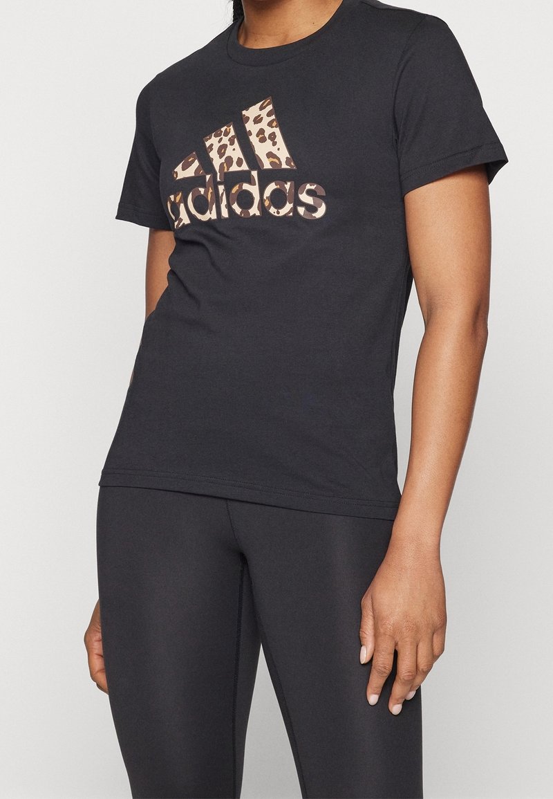 Svart bomulls-t-shirt med ett leopardmönstrat Adidas-logotyp över bröstet, korta ärmar och en figursydd design.