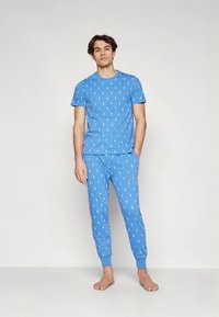 Světlomodrá sada pyžama z měkké látky; tričko s kulatým výstřihem a krátkými rukávy, zdobené malými bílými motivy, ke kterým ladí kalhoty.