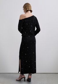 Top negro de punto con hombros descubiertos combinado con una falda a juego, ambos con adornos plateados y aberturas laterales. Incluye sandalias de tiras.