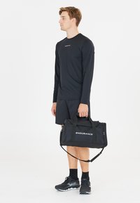 Musta duffel-laukku, jossa on valkoisilla kirjaimilla painettuna "ENDURANCE". Kestävästä kankaasta valmistettu, varustettu kahdella käsikahvalla ja irrotettavalla olkahihnalla.