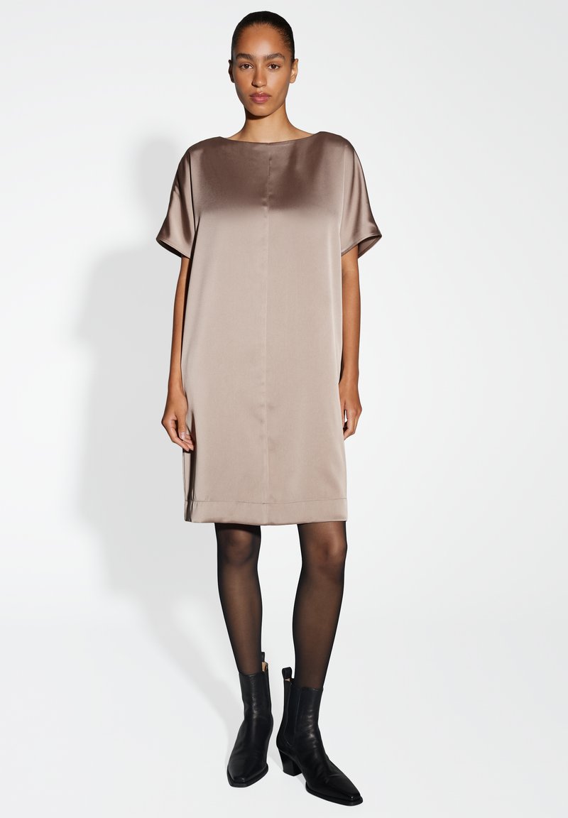 Tailliertes satin taupe Kleid mit einem Boot-Ausschnitt, kurzen Ärmeln und schlichter Silhouette. Kombiniert mit schwarzen Knöchel-Stiefeln und transparenten schwarzen Strumpfhosen.