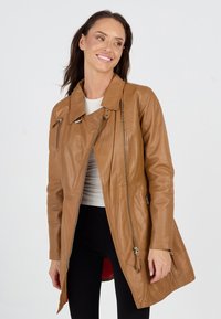 Tanfarbene Lederjacke mit asymmetrischem Design, Hochkragen, silbernen Reißverschlüssen und Seitentaschen. Glatte Textur und figurbetonte Form.