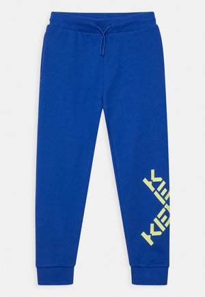 Pantalons de survêtement bleus en mélange de coton, dotés d'une cheville ajustée et d'un grand logo jaune imprimé en diagonale sur le bas de la jambe.