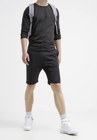 Černá dlouhá tričková košile a šortky z měkké, elastické látky, doplněné bílými teniskami a šedým batohem. Jednoduchý design, bez vzorů.