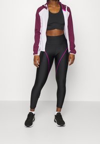 Ensemble de vêtements de sport comprenant une veste zippée bordeaux et blanche, un crop top noir et des leggings noirs avec des lignes d'accent violettes. Comprend des baskets noires.