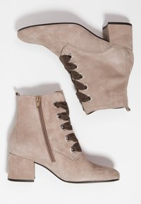 Botines de ante beige con tacón ancho, cremallera lateral y detalles en encaje marrón a través de ojales plateados. Diseño de punta afilada.
