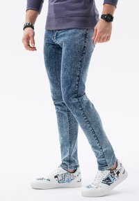 Slim fit jeans i en blekt blå denimstruktur, kombinerat med vita sneakers med grafiskt mönster i blå och svarta accenter.