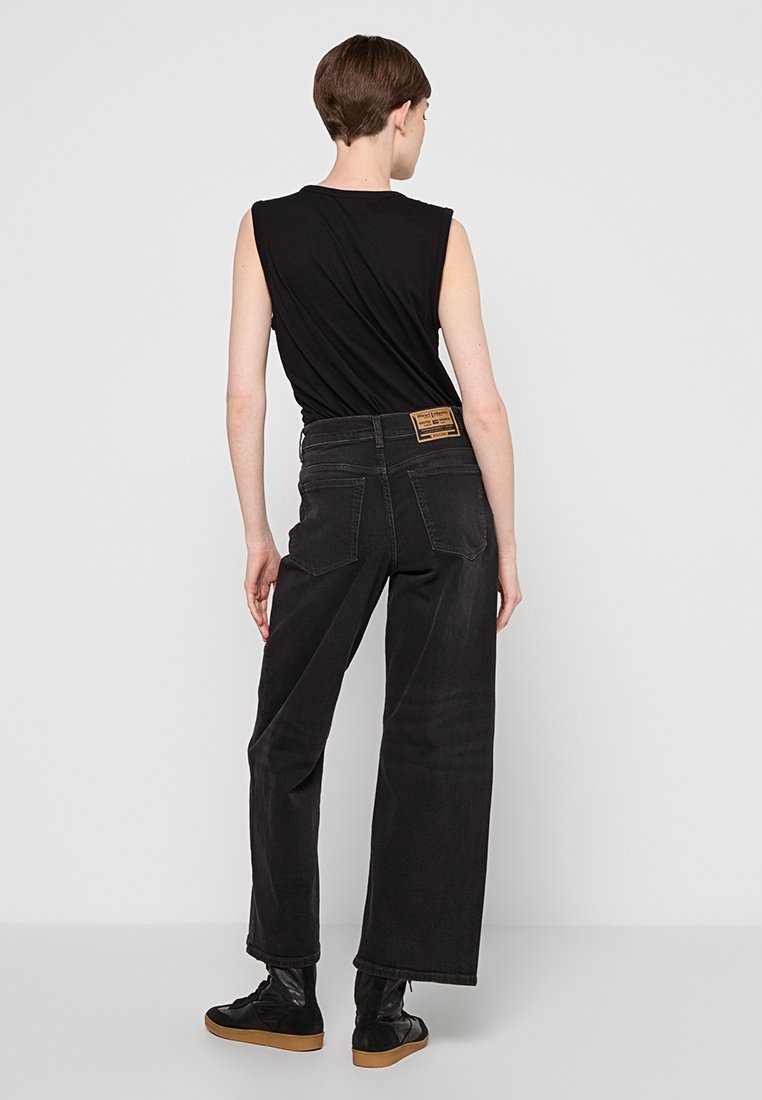 Jeans in denim neri a gamba larga con vita alta, etichetta in pelle sul retro e una superficie liscia. Abbinati a un top senza maniche nero.