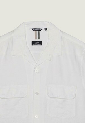 Camicia bianca a maniche corte con bottoni, due tasche con patta sul davanti, colletto alla coreana e etichette del marchio cucite all'interno del collo.