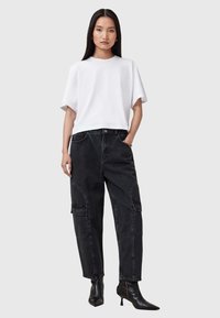 T-shirt bianco a maniche corte abbinato a jeans cargo neri a vita alta, caratterizzati da ampie tasche e una silhouette dritta. Stivali neri con tacco.